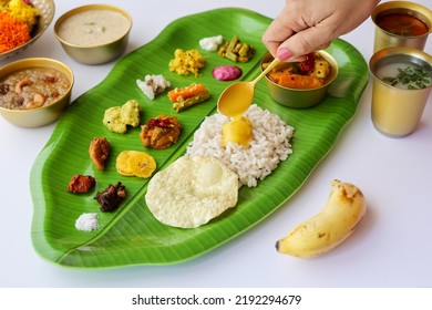 Women pouring ghee totraditional Onam sadhya rice Sambar, Rasam, parippu dal curry ghee Pappadom Payasam on banana leaf Onam Vishu Pongal Diwali festival vegetarian food Kerala Tamil Nadu South India. - Shutterstock ID 2192294679