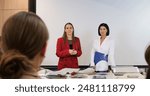 Women in professional settings navigate conflict during presentation. Tension between two colleagues underscores challenges of maintaining friendships at work amidst professional rivalries.