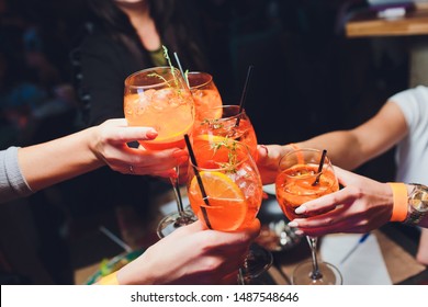 women raising a glasses of aperol spritz at the dinner table.