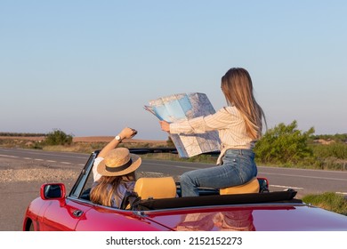 Women reading and holding a map sitting in red convertible car on remote road at sunset with golden light