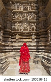 A women in a red saree looking at carvings on the walls of the Western Group of temples of Khajuraho, famous for their erotic sculptures, India.