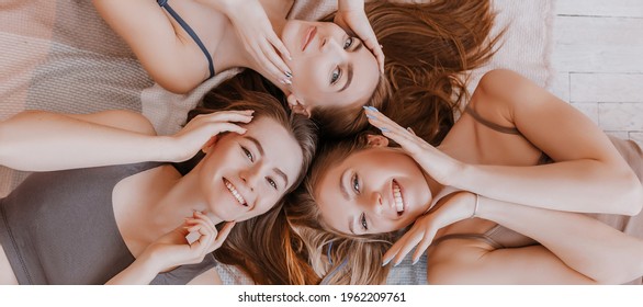 Women rest and have fun. Girlfriends laugh at home lying on the floor on pillows. Tree girls make homemade face and hair beauty masks. Women take care of youthful skin.