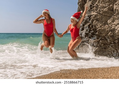 Women Santa hats ocean play. Seaside, beach daytime, enjoying beach fun. Two women in red swimsuits and Santa hats are enjoying themselves in the ocean waves and raising their hands up. - Powered by Shutterstock