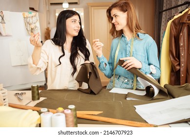 Women Seamstresses Sweep Away, Sew Fabric, Details Of Future Clothes. Happy, Smiling. Fashionable Sewing Studio Indoors.