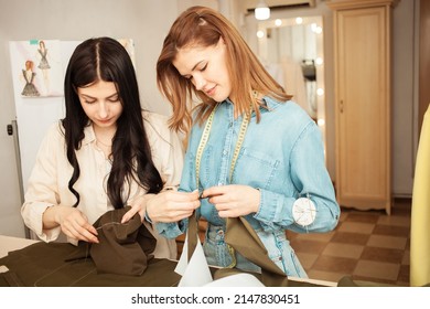 Women Seamstresses Sweep Away, Sew Fabric, Details Of Future Clothes. Happy, Smiling. Fashionable Sewing Studio Indoors. Portrait