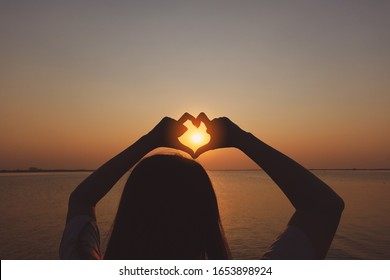 women show heart shape by hand with the sunset on the beach