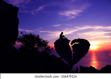 Women sit on broken heart-shaped stone on a mountain with purple sky sunset background.Silhouette Valentine background concept.
