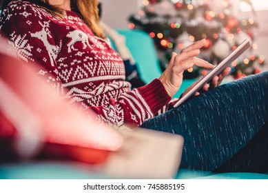 Women sitting on the blue sofa by the christmas tree and using tablet  - Powered by Shutterstock