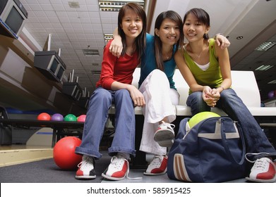 Women Sitting Side By Side In Bowling Alley, Smiling At Camera