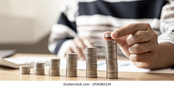 Women are stacking coins on top of the coin pile on the highest row. Placing coins in a row from low to high is comparable to saving money to grow more. Money saving ideas for investing in funds. - Shutterstock ID 1934382134