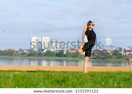 women stretching in the park near lake. city scape on background. morning exercises. young caucasian girl doing yoga, Natarajasana, standing in Lord of the Dance pose. fitness and healthy lifestyle.