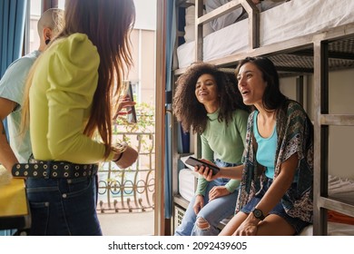 Women students talking about a social network content on the smartphone screen sitting on bunk bed of an hostel room