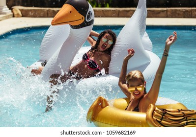 Women swimming in pool with inflatable toys. Females friends enjoying in a pool on their summer vacation.