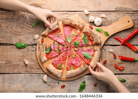 Women taking slices of tasty pizza from board on table