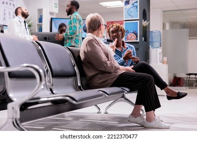 Women talking each other at hospital waiting area. African american man talking to general practitioner. People awaiting in sanatorium admissions section. Elderly lady explaining condition to girl.