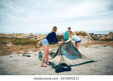 Women, tent setup and camping at beach for vacation trip, outdoor and together for bonding. Girl, travel and adventure in nature for shelter, friends activity or campsite under cloudy sky for holiday - Powered by Shutterstock