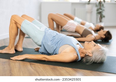 Women three generations doing glute bridge exercise, dvi pada pithasana pose, working out in yoga studio - Powered by Shutterstock