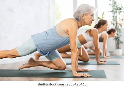 Women three generations practicing yoga positions during group training in fitness center, performing stretching asana Urdhva Mukha Shvanasana - Powered by Shutterstock