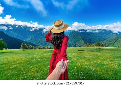 Women tourists holding man's hand and leading him to green pasture and flowers near snow mountain in Georgia.