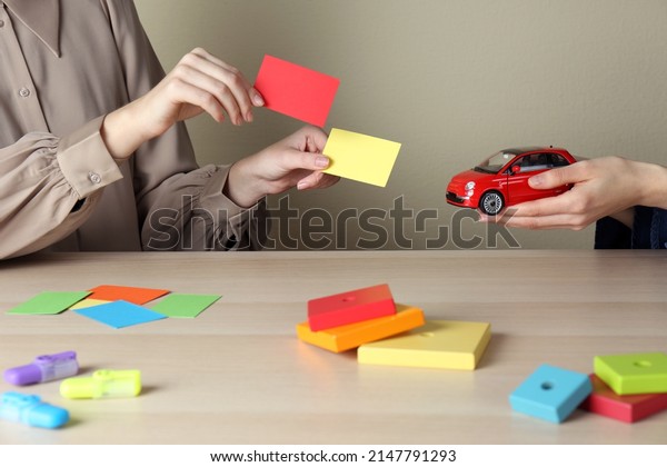 Women with toy car and color papers at\
wooden table indoors, closeup. ABA therapy\
concept