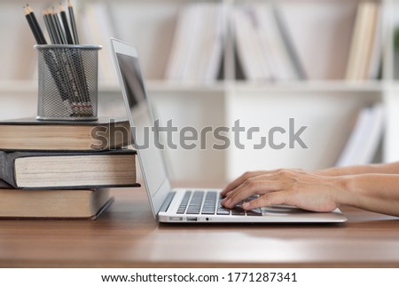 women using laptop computer with book stack on desk in library. e-book digital technology and e-learning class concept.