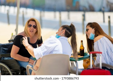 Women Using Surgical Masks Checking A Smart Phone While Having A Snack At An Outdoor Terrace On An Out Of Focus Background. New Lifestyle And Disability Concept.