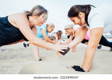 Women of various ages doing fitness workouts in class exercise with coach on beach. Ladies doing paired plank exercises and high-fiving each other. Sport for health and wellbeing. Active lifestyle - Powered by Shutterstock