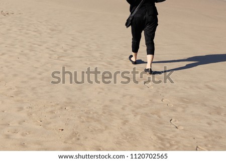 A women walking on the beach and leaving footprints behind. This image can be used to represent solo travel. 