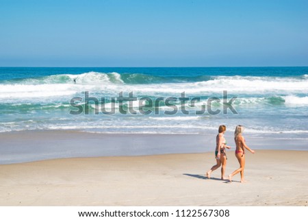 Women walking on the beach on a summer day and a surfer riding a wave background