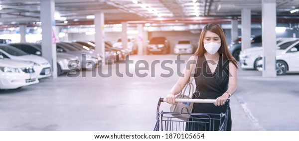 women wearing face mask with shopping car on\
parking car of the\
supermarket.