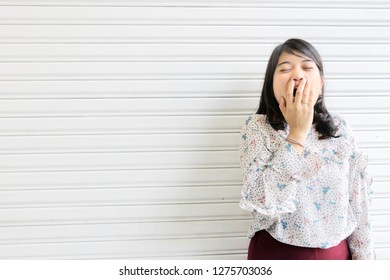 Women Who Are Yawning With Drowsiness During The Daytime, The Background Is A White Wall. Drowsiness Caused By Hard Work And Insufficient Rest.