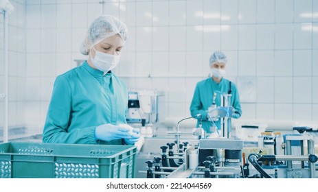 Women Work On The Capsule Packaging Line And Put The Finished Product Into A Box. Bottle Filling Machine. Bottles On A Conveyor Belt. Production Line Of Pharmaceutical Manufacturing