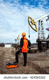 Women Worker In The Oil Field, With Wrenches In A Hands, Orange Helmet And Work Clothes. Industrial Site Background.