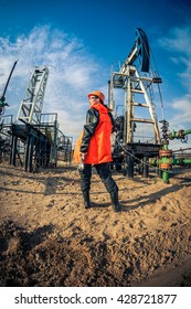 Women Worker In The Oil Field, With Wrenches In A Hands, Orange Helmet And Work Clothes. Industrial Site Background.