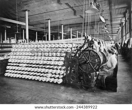 Women working at textile machines, beaming and inspecting yarn, at the American Woolen Company, Boston. The beaming process prepares the warp, the lengthwise fibers of a woven fabric. Ca. 1910.