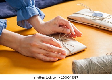 women wrapping gift. A parcel wrapped in paper and tied with rough twine on yellow table - Powered by Shutterstock