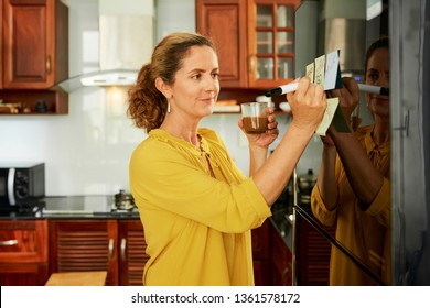 Women Writing Shopping List On Fridge