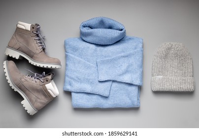 Women's Autumn Or Winter Outfit. Knitted Blue Sweater, Hat And Suede Boots. Gray Background. Flat Lay.