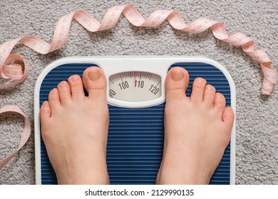 Women's bare feet on floor scales and measuring tape, weight 100-110 kilograms, top view. The idea of obesity, weight loss and excess weight.