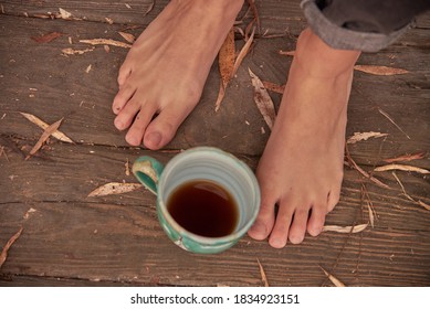 Women's bare feet stand on a wooden floor covered with autumn leaves. A ceramic Cup with a drink stands next to the feet. - Powered by Shutterstock