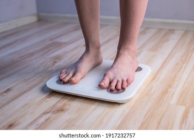 Women's bare feet stand on electronic scales on the wooden floor. The concept of fitness and weight loss tracking
