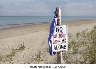 Women's Bathing Suit Hanging From "No Skinny Dipping Alone" Sign at Beach 