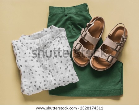 Women's bermuda shorts, cotton blouse, leather sandals on a light background, top view