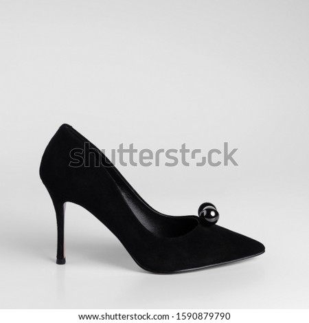 Womens black suede heeled shoes with a pearl toe decorative element. Close-up side view studio shot. On a white background for a catalog