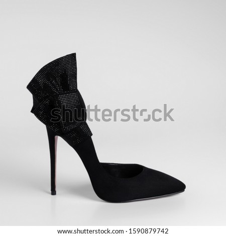 Womens black suede high heel shoes with a decorative bow element with black rhinestones on heel. Close-up side view. On a white studio background with natural shadows.