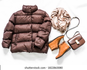 Women's brown down jacket, cashmere scarf, leather shoulder bag, oxford suede boots on a light background, top view. Autumn, winter women's clothing fashion concept                     