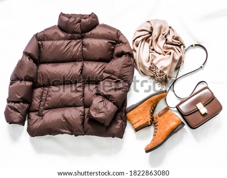 Women's brown down jacket, cashmere scarf, leather shoulder bag, oxford suede boots on a light background, top view. Autumn, winter women's clothing fashion concept                     