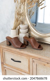Women's brown leather clogs stand at the mirror in a bright interior.