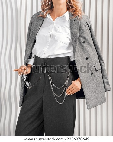 Women's Business suit. Gray jacket, high-waisted palazzo trousers, black belt with silver chain. White shirt with chest pocket.