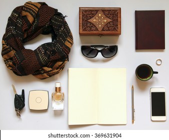 Women's Casual Accessories On White Background: Brown Scarf, Sunglasses, Powder Compact, Empty Sketchbook, Pen, Car Keys, Perfume, Wallet, Cellphone, Ring, Wooden Box